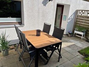 A wooden patio table with chairs, a small potted plant, and a sign on the wall.