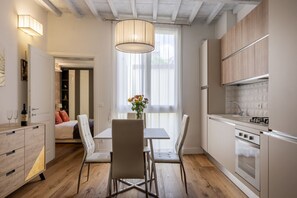 Eine moderne Küche mit Holzschränken, ein Essbereich mit Tisch und Stühlen und ein großes Fenster mit Vorhängen.