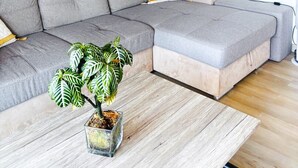 Ein modernes Wohnzimmer mit einem Ecksofa, einem Couchtisch, einer Zimmerpflanze und einem großen Fenster.