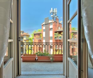 Ein offener Balkon mit Blick auf angrenzende Gebäude, einem Metallzaun und Topfpflanzen.