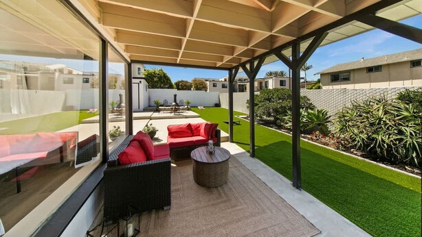 A covered outdoor patio with a sofa and a round table, a lawn, and a view of neighboring houses. - 1 Bedroom Steps From Beach and Carlsbad Village (Carlsbad)
