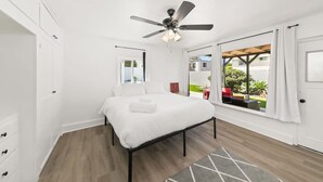 A bedroom with a bed, a ceiling fan, a window with a view of the outside, and a door. - 1 Bedroom Steps From Beach and Carlsbad Village (Carlsbad)