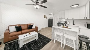A modern living room with a brown sofa, white coffee table, and a ceiling fan. - 1 Bedroom Steps From Beach and Carlsbad Village (Carlsbad)