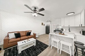 Ein modernes Wohnzimmer mit einem braunen Sofa, einem weißen Couchtisch und einem Deckenventilator.