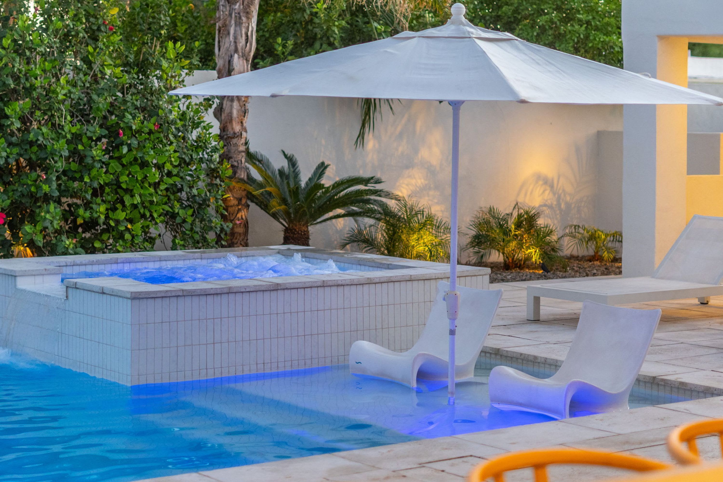 A swimming pool with a hot tub, lounge chairs, and an umbrella.