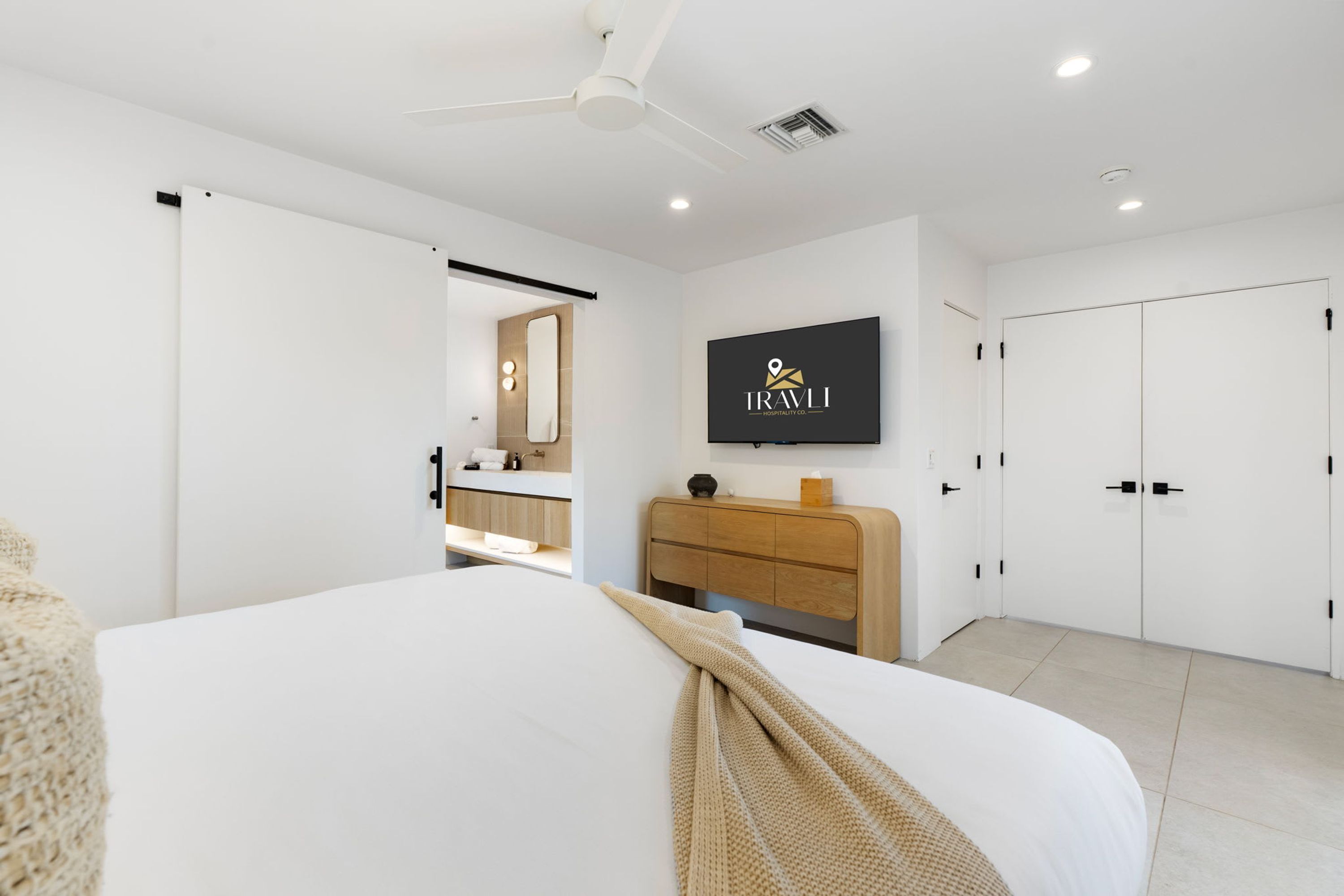 A modern hotel room with a bed, a TV mounted on the wall, a ceiling fan, and a wardrobe.