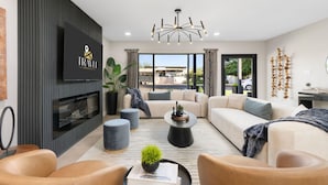 A modern living room with a flat-screen TV, a fireplace, a sofa, a coffee table, and a chandelier. - NEW The Barrington Ultra-luxe Designer Estate (Scottsdale)