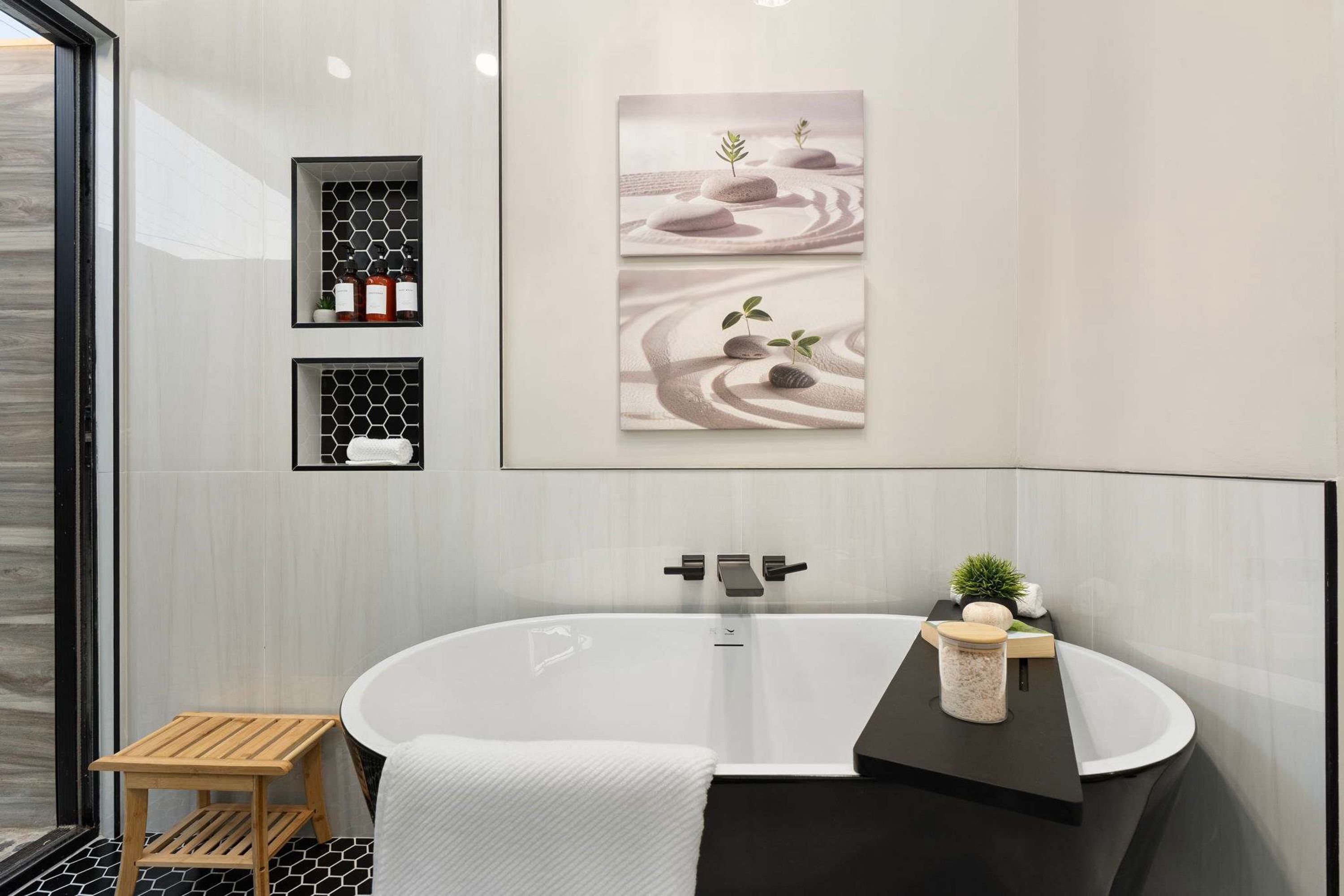 Een moderne badkamer met een vrijstaand bad, een houten krukje en een klein plankje met een plant.