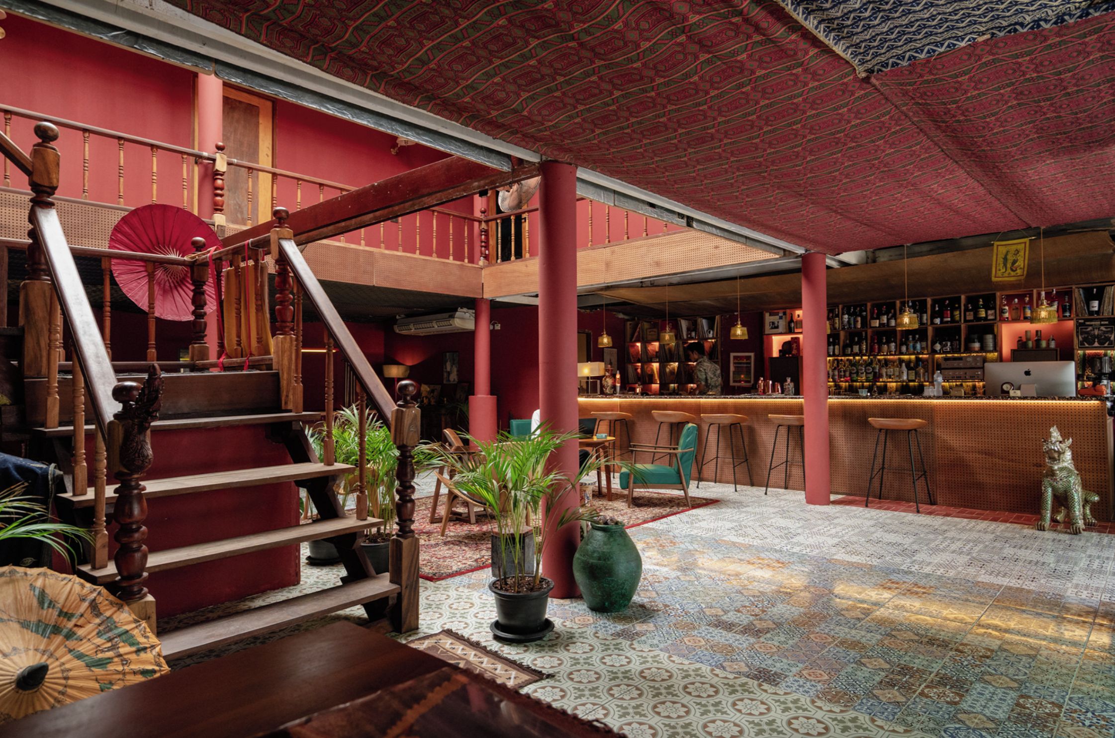 A bar area with a red ceiling, wooden staircase, and a variety of plants.