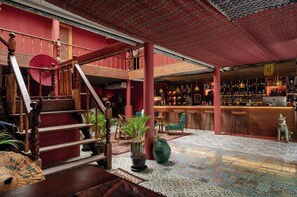 Uma área de bar com teto vermelho, escada de madeira e diversos vasos de plantas.