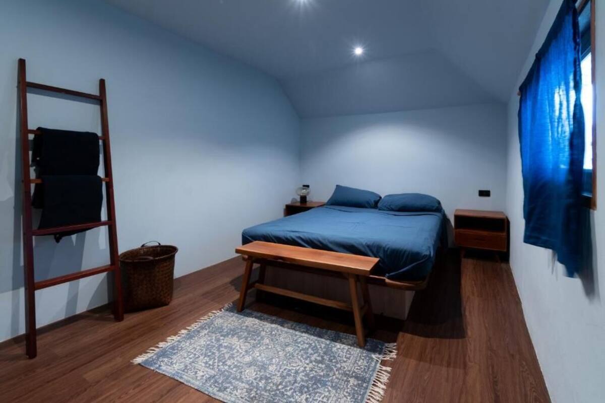 A bedroom with a bed, wooden bench, ladder, and a small table.