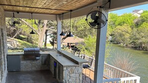 Un patio techado con una parrilla, asientos al aire libre y vistas a un lago.