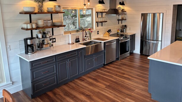 Una cocina moderna con armarios oscuros, electrodomésticos de acero inoxidable y suelo de madera.