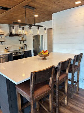 A modern kitchen with a large island, stainless steel appliances, and wooden chairs.