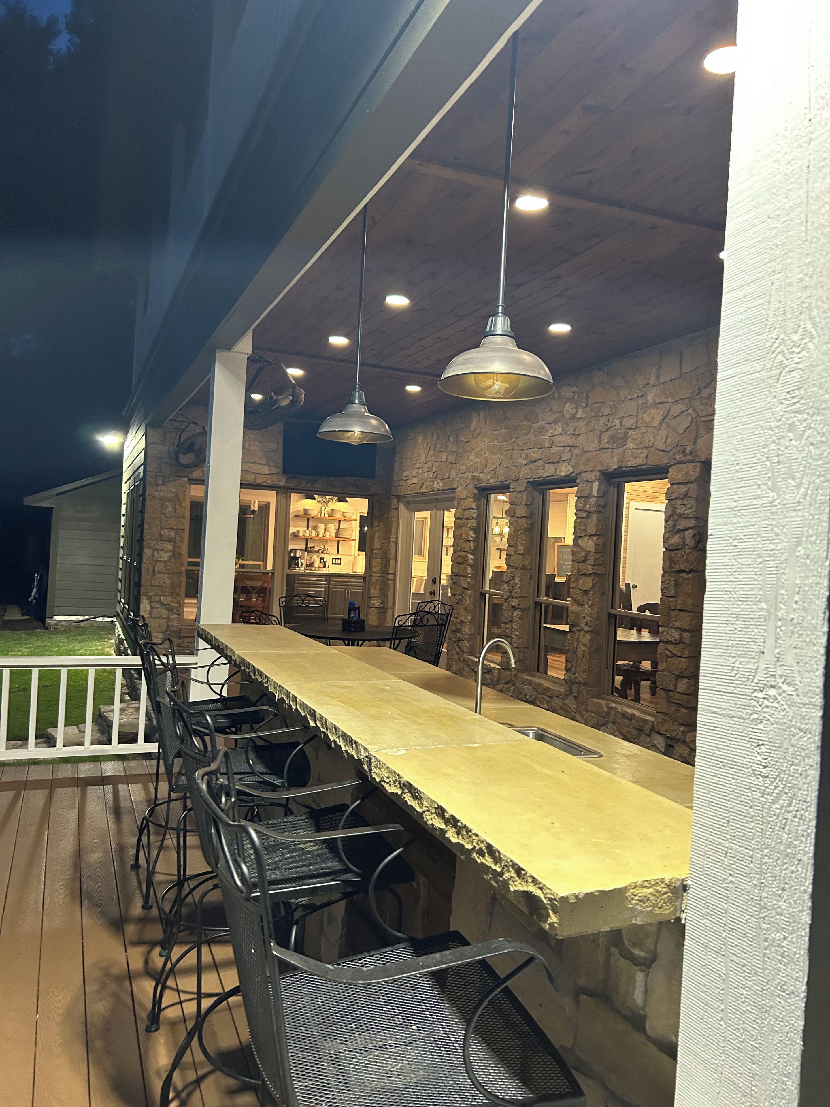 An outdoor bar area with a stone wall, metal bar stools, and pendant lighting.