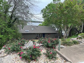 A house with a dark exterior, a front porch, and a garden with pink flowers.