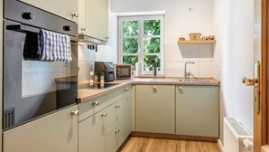 Una cucina compatta con forno a incasso, microonde e lavello. Una finestra offre vista sul verde circostante.