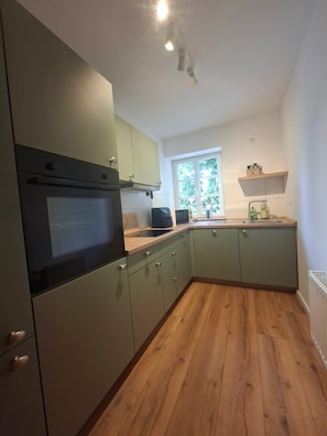 Cocina con horno empotrado, microondas y ventana con vistas a zonas verdes.