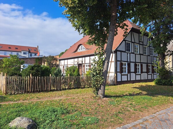 Ein traditionelles Fachwerkhäuschen mit geneigtem Dach, umgeben von einem Holzzaun und einer Rasenfläche.