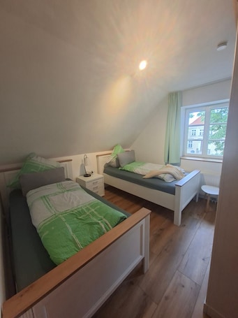 A bedroom with two beds, a nightstand, a lamp, and a window with a view of a building outside.. Zeitlos Wriezen 3 – Cozy Apartment for 4 with Garden, Parking, and Self-Check-in