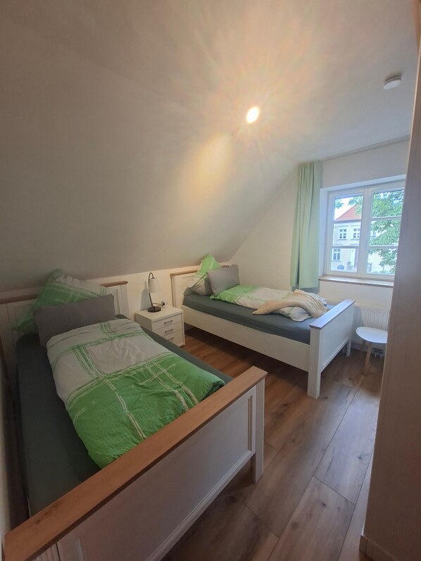 A bedroom with two beds, a nightstand, a lamp, and a window with a view of a building outside.