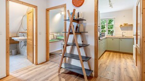 Una stanza con una scaffalatura a scaletta in legno, una sveglia e vista sulla cucina e il bagno.
