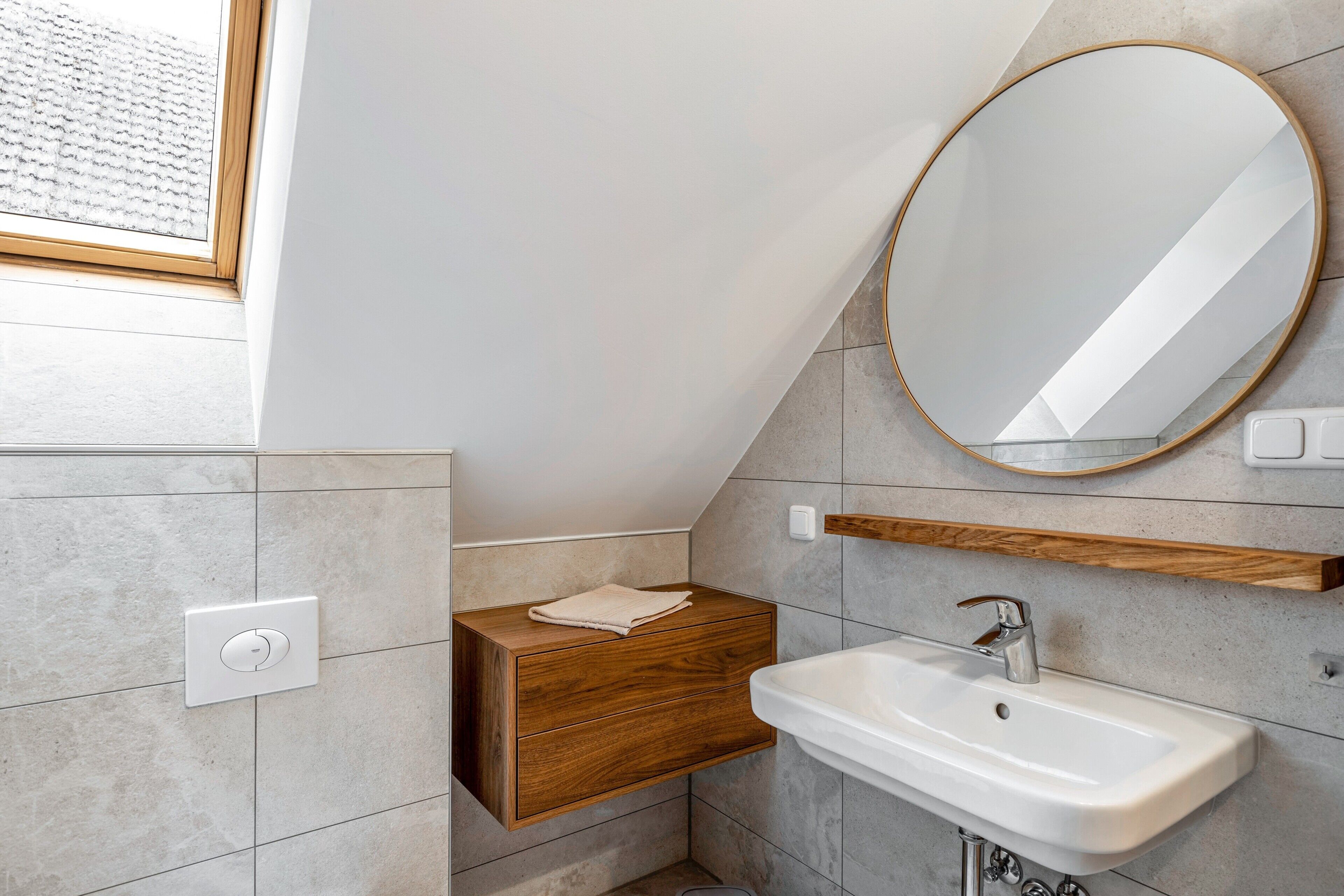 A modern bathroom with a built-in sink, a wooden vanity, a round mirror, and a window.