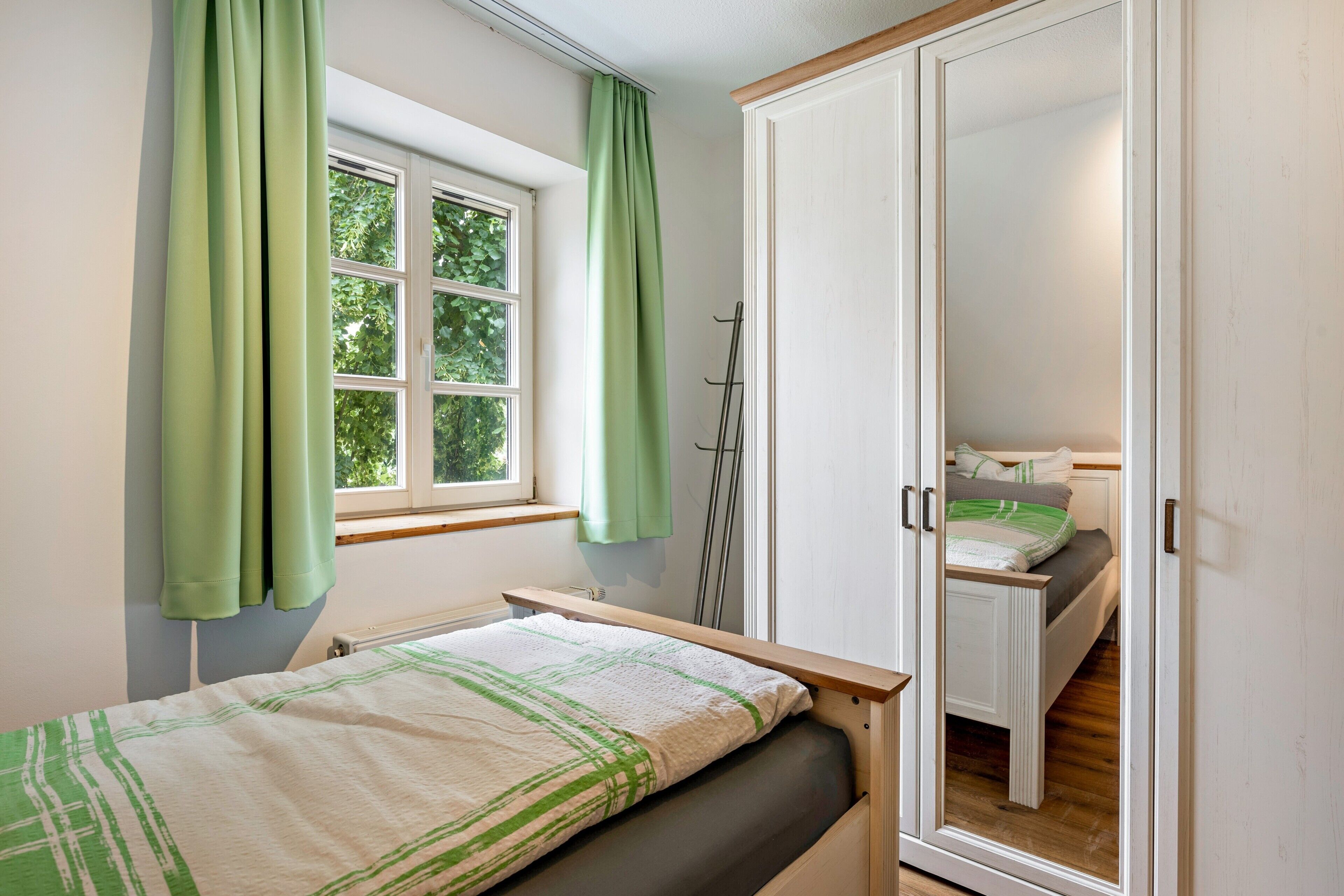 A bedroom with a bed, a window with curtains, a wardrobe, and a mirror.