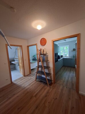 Ein Zimmer mit Holzboden, einer Holzleiter, einer Uhr und Blick in einen weiteren Raum mit einem Fenster.