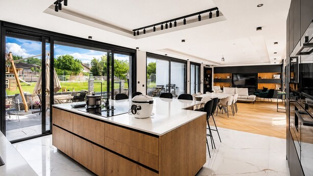 Eine moderne Küche mit einer großen Kochinsel, ein Essbereich mit Tisch und Stühlen sowie ein Wohnzimmer mit Sofa und Fernseher.