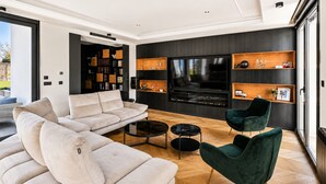 Ein modernes Wohnzimmer mit Sofa, zwei Sesseln, einem Couchtisch, einem Fernseher und integrierten Regalen.
