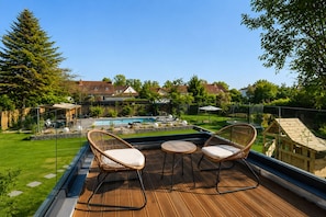 Une terrasse en bois, agrémentée de chaises en osier et d’une petite table, donnant sur une piscine et une pelouse bien entretenue.