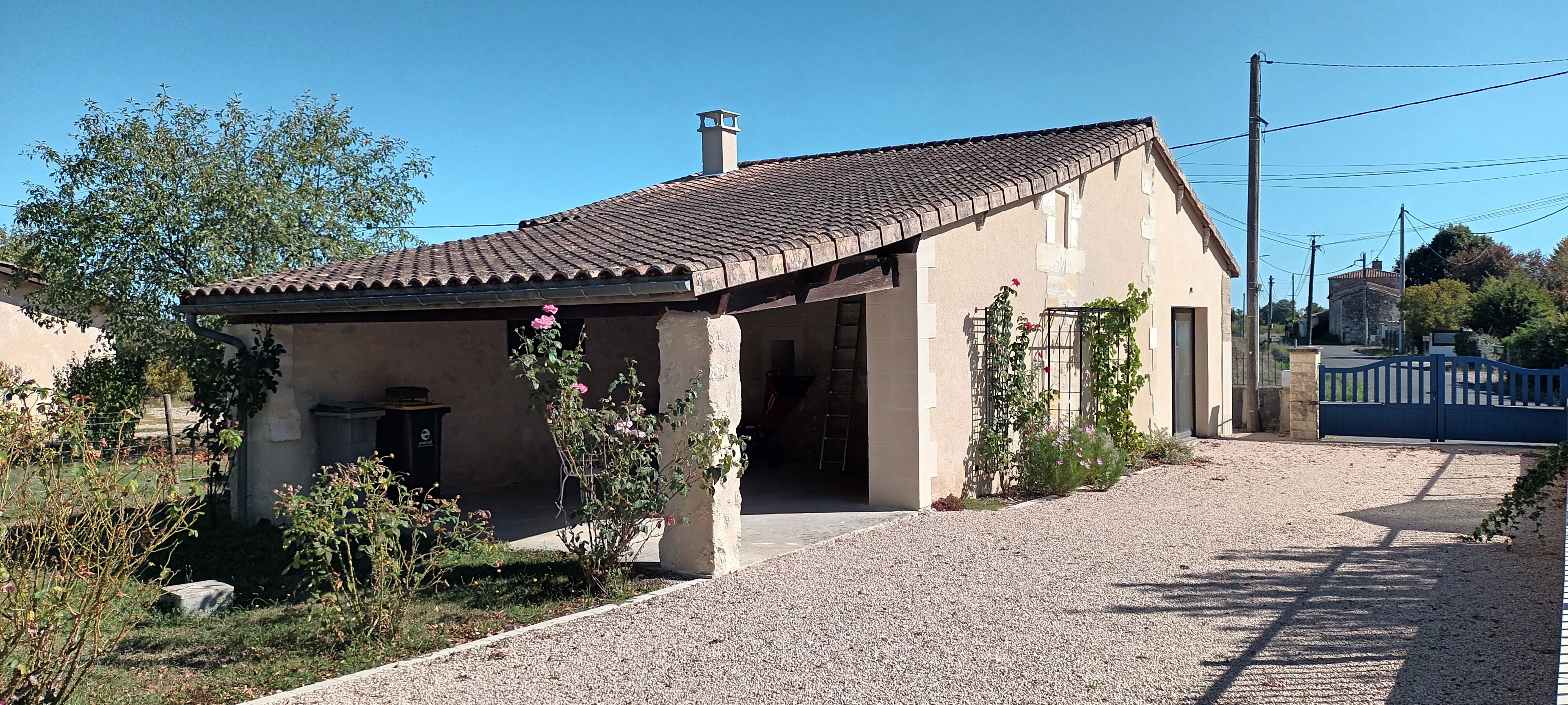 A single-story building with a tiled roof, a gravel driveway, and a metal gate.