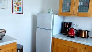 Eine Küche mit einem weißen Kühlschrank, Holzschränken, einer Edelstahl-Mülltonne und einer Kaffeemaschine.