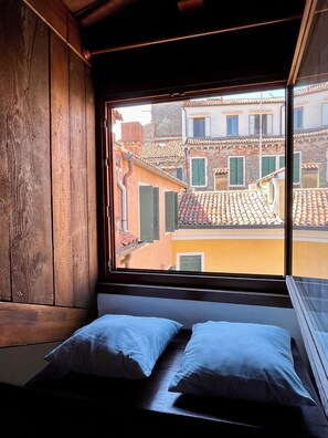 A room with a window overlooking a street with buildings. There is a bed with pillows. - La Casetta—2-room apartment in the heart of Venice (Venezia)