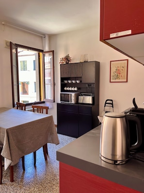 A compact kitchen with a dining area, a microwave, a kettle, and a cabinet with kitchenware. - La Casetta—2-Bedroom Apartment in the Heart of Venice (Venezia)