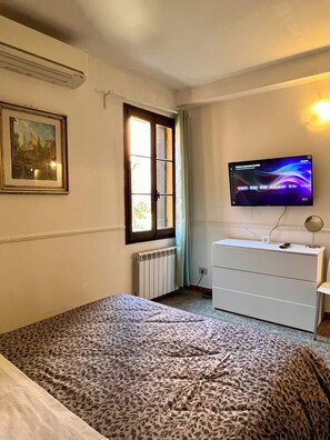 A bedroom with a bed, a dresser, a television, a radiator, and a window. - La Casetta—2-room apartment in the heart of Venice (Venezia)