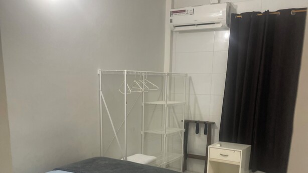 Ein Schlafzimmer mit einem Bett, einem weißen Kleiderschrank, einem kleinen Tisch, einer Kleiderstange und einer Klimaanlage.