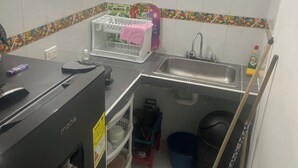 Eine kleine Küche mit Spüle, Geschirrgestell, einem Mop und Reinigungsmitteln.