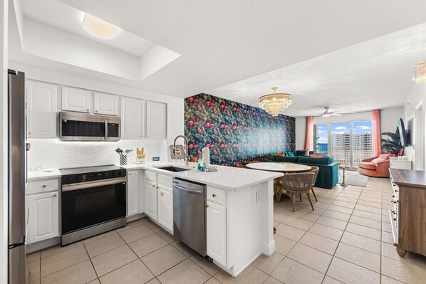 A modern kitchen with white cabinets, stainless steel appliances, and a colorful tropical mural. - Emerald Flamingo 902 | Gulf Views + Private Beach (Miramar Beach)