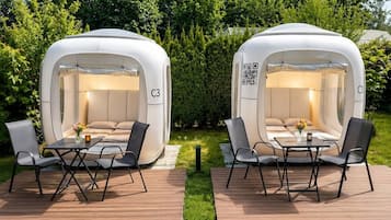 Deux cabanes extérieures aménagées pour dormir, portant les numéros C1 et C3, chacune équipée d’une table et de chaises, et installées sur une terrasse en bois avec de l’herbe en arrière-plan.