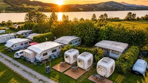A campsite with RVs and mobile homes, a gravel path, and a lake with mountains in the background. - Cubes am Irrsee - Self Check-In (Fischhof)