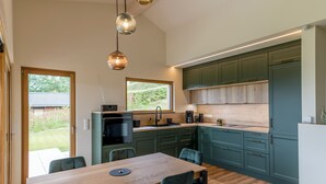 A modern kitchen with wooden cabinets, a dining table with chairs, and pendant lighting.