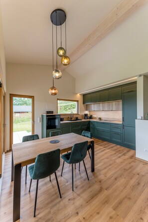Une cuisine moderne avec des meubles en bois, une table à manger avec des chaises et des luminaires suspendus.
