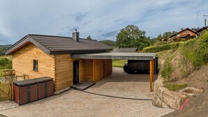 A modern log cabin with a covered outdoor area, a wooden deck, and a view of the surrounding countryside.