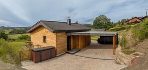 Une cabane en rondins moderne dotée d’un espace extérieur couvert, d’une terrasse en bois et offrant une vue sur la campagne environnante.