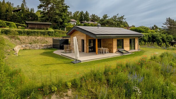 A modern house with a patio, a covered outdoor seating area, and a view of the surrounding greenery.