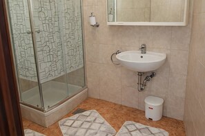 Ein Badezimmer mit Duschkabine aus Glas, einem Waschbecken, einer Toilette und Teppichen mit Muster auf dem Boden.