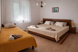 Ein Doppelbett mit Holz Kopfteil, ein Nachttisch mit Lampe, ein Fenster mit transparenten Vorhängen und ein kleines Bild an der Wand.