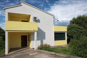 Ein zweistöckiges Gebäude mit einer gelb-weißen Fassade, einem Balkon und einer Klimaanlage.